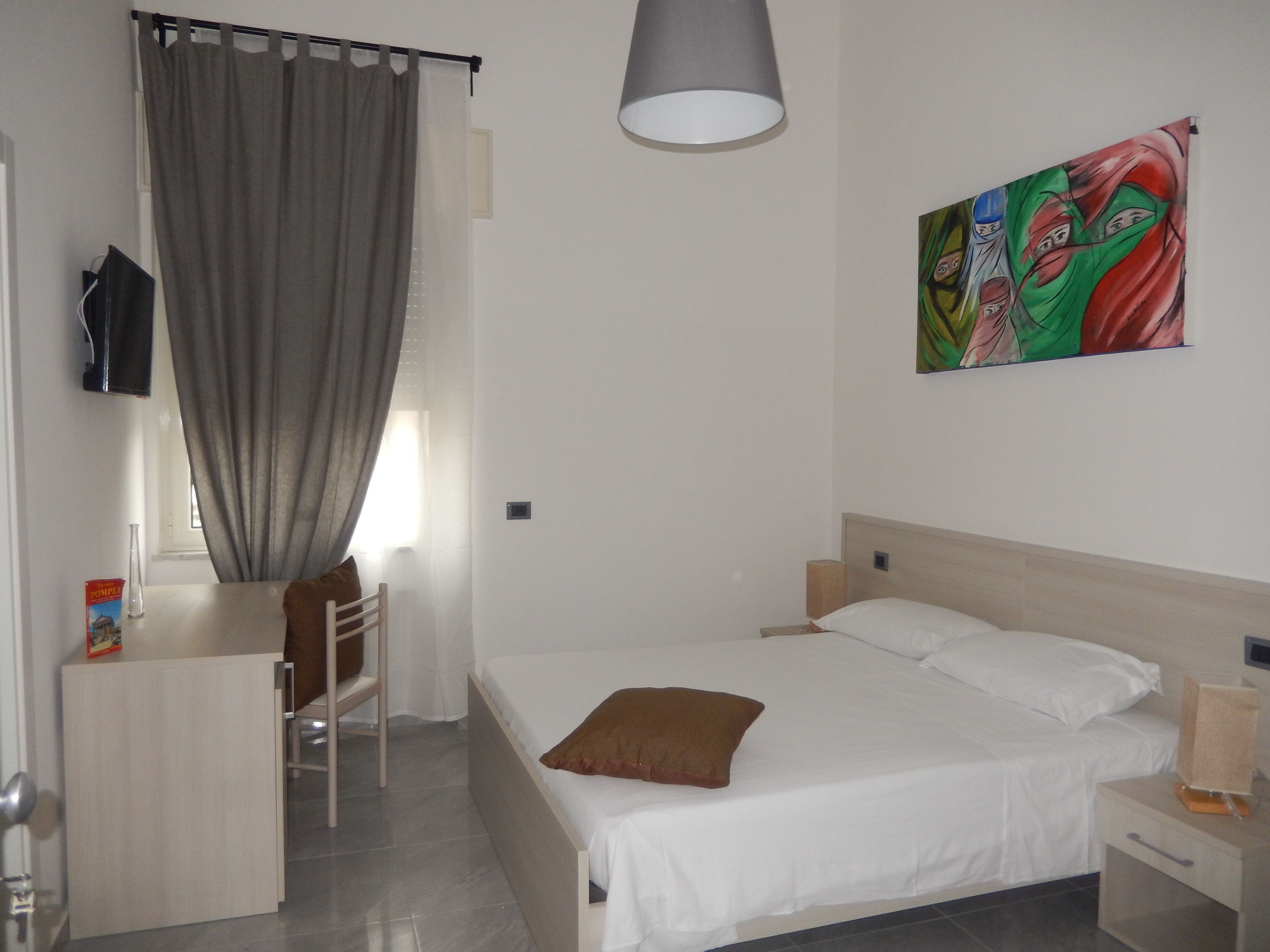 A bedroom with a bed, a desk, a chair, a lamp, and a painting on the wall.