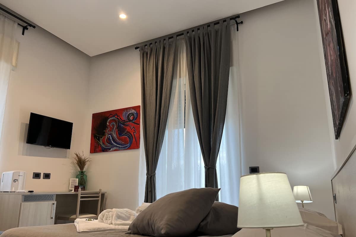 A hotel room with a bed, a desk, a TV, and a painting on the wall.
