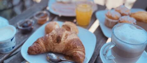 A table with breakfast items including croissants, a glass of coffee, and a packet of Dorate biscuits.