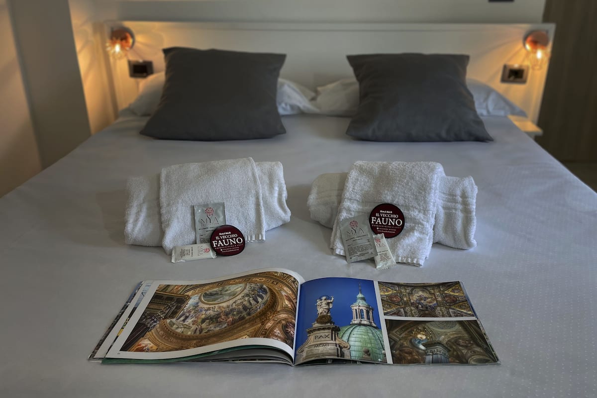 A neatly made bed with two pillows, a pair of towels, and a brochure on the bed.
