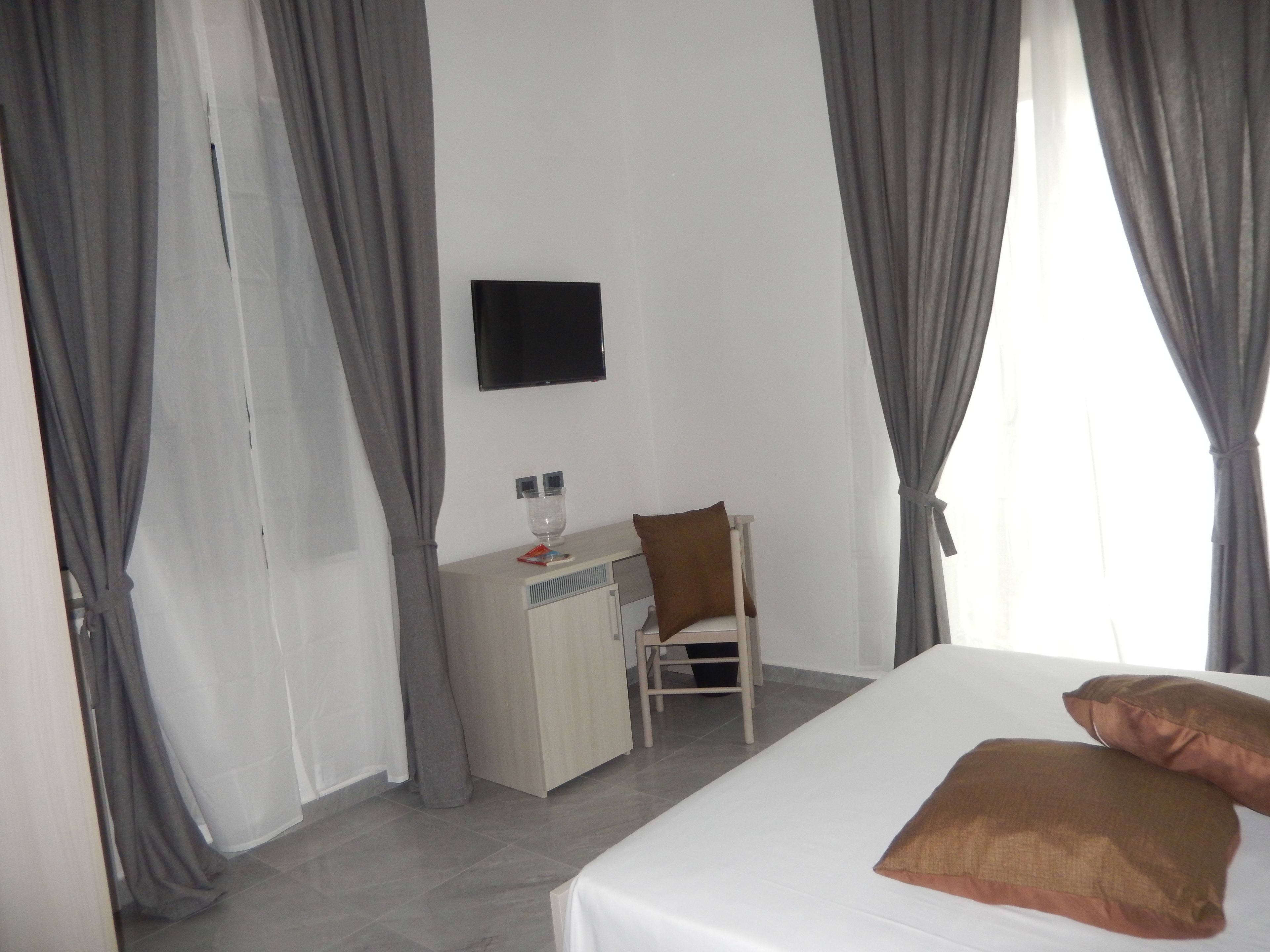 Una habitación de hotel con cama, escritorio, silla, televisor y cortinas.