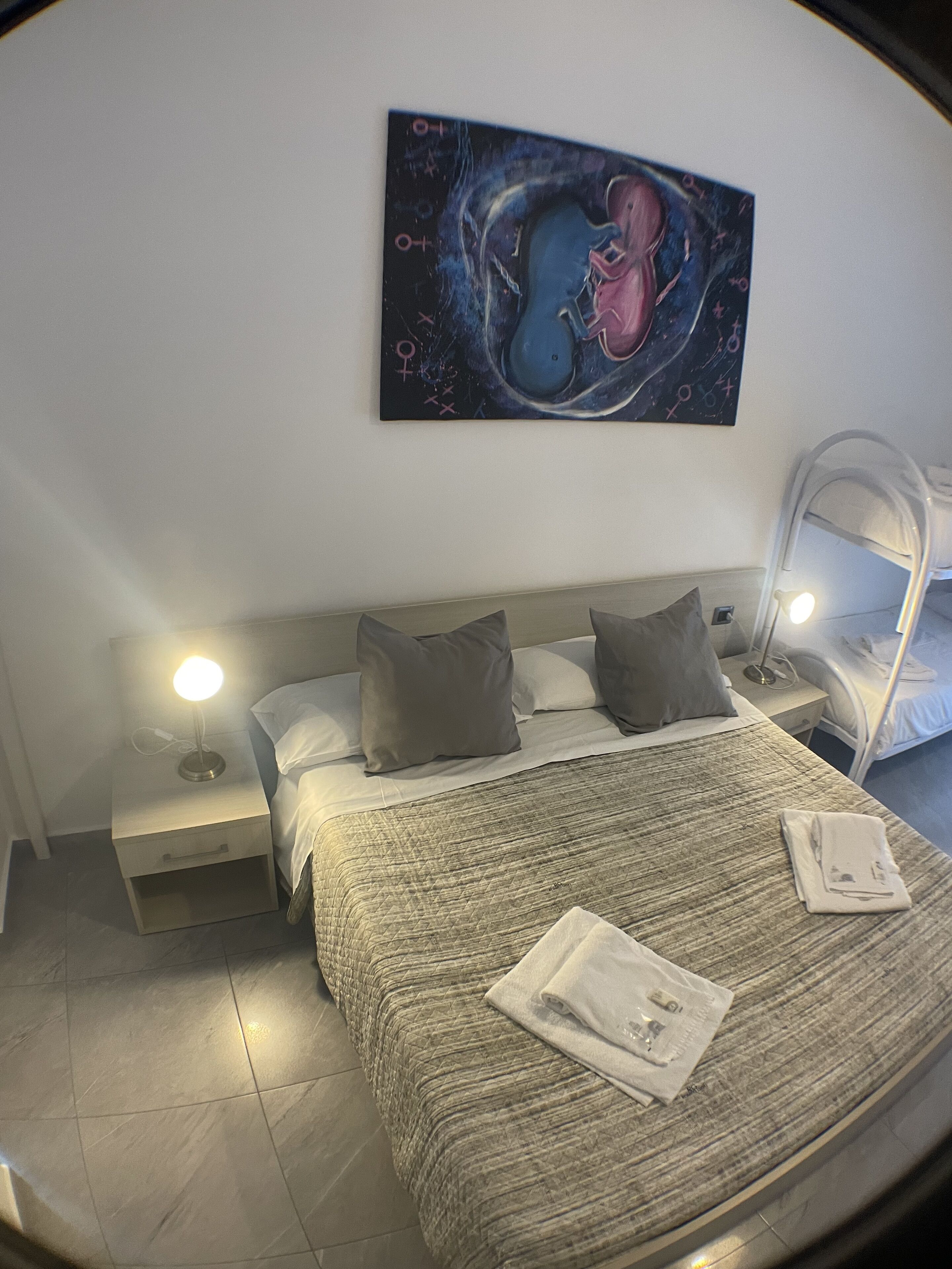 Un dormitorio con una cama, dos mesitas de noche con lámparas, una litera y una obra de arte en la pared.
