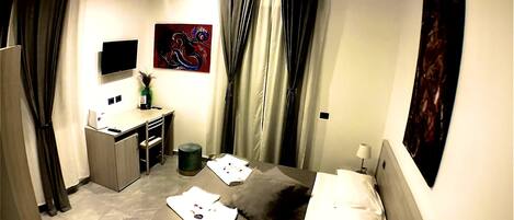 A hotel room with a bed, a desk, a chair, a TV, and artwork on the walls.