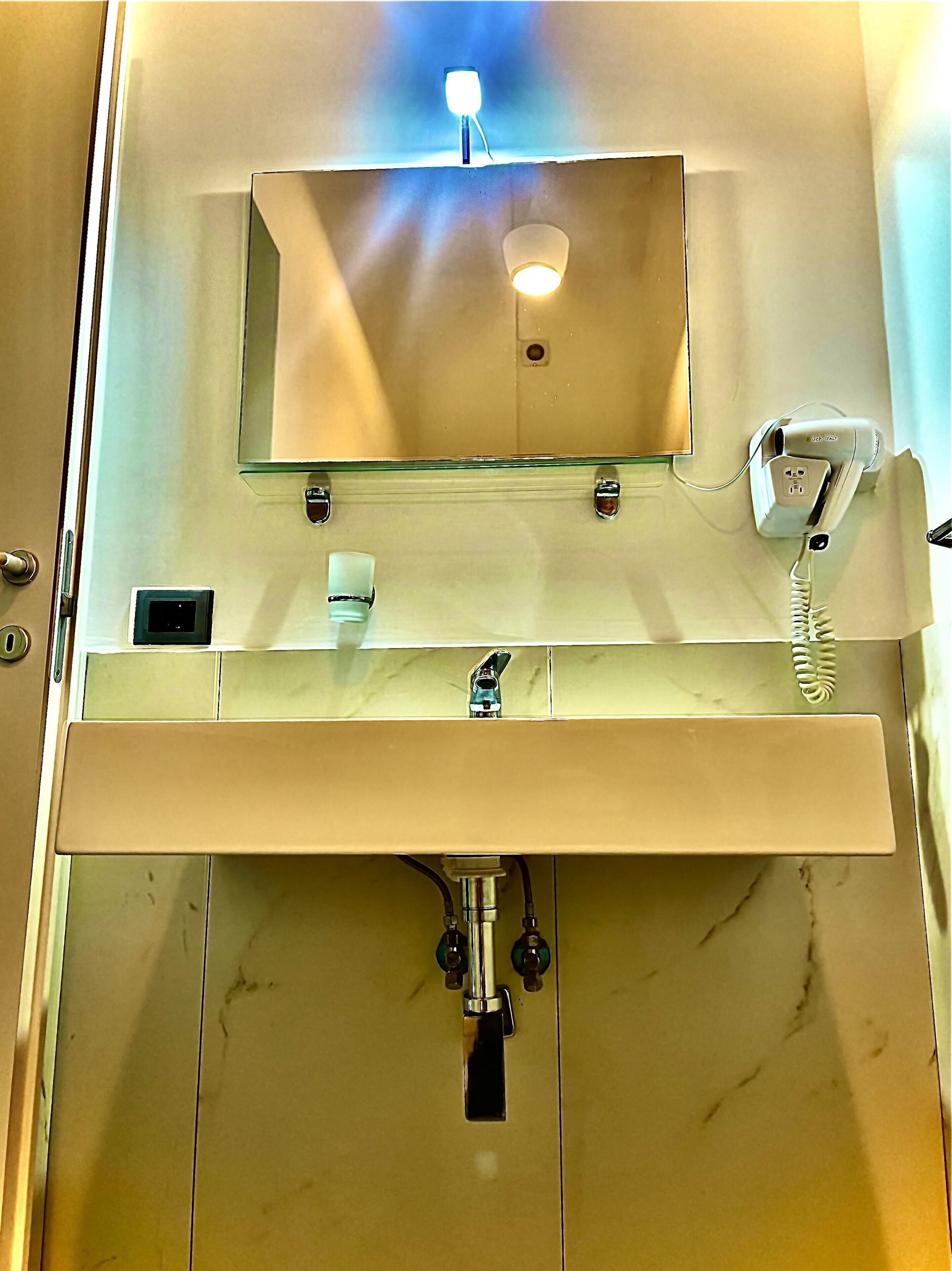 Ein Badezimmer mit einem Tresen mit Glasabdeckung, einem Spiegel, einem Handyladekabel und einem Wasserhahn.