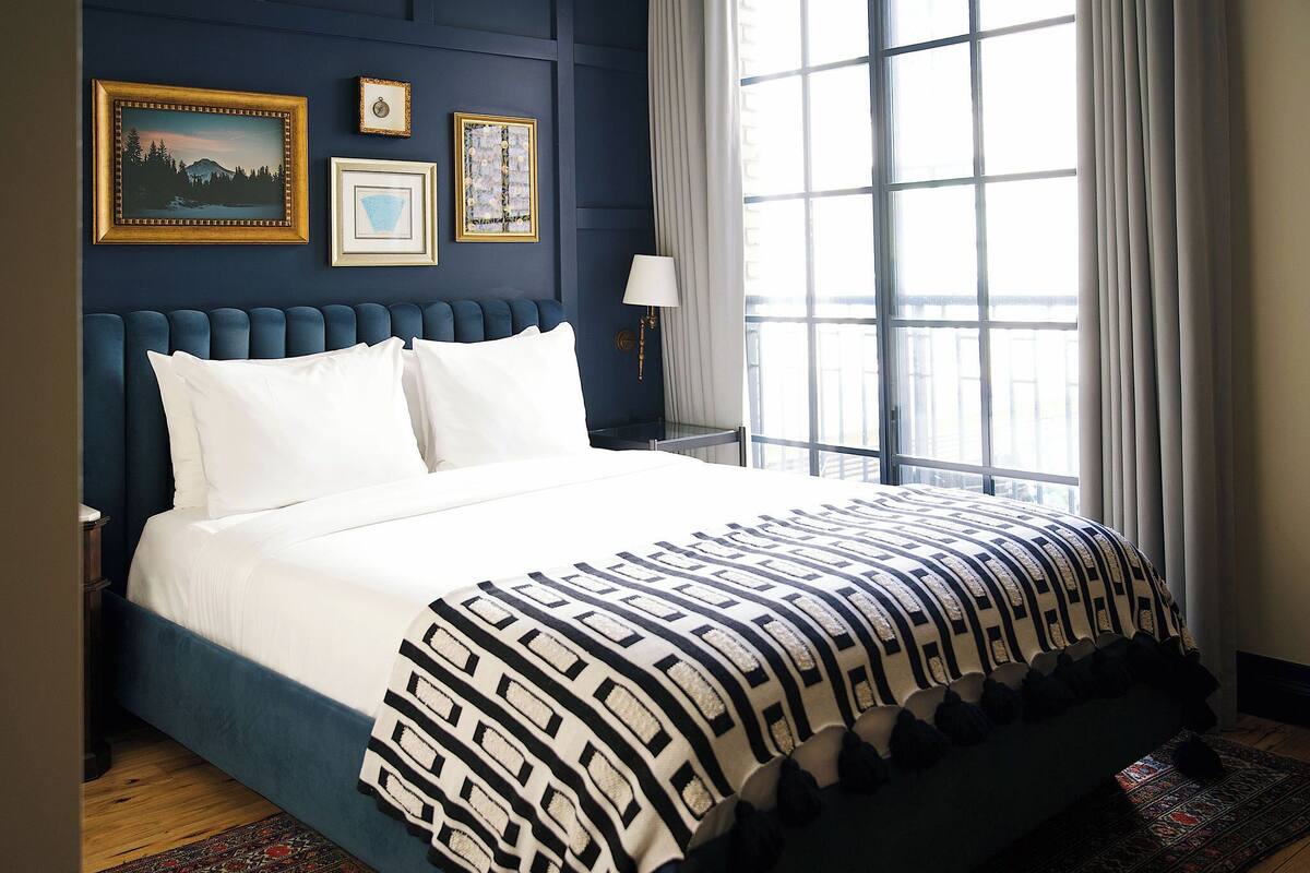 A bed with a patterned bedspread, a nightstand, a lamp, and framed pictures on the wall.