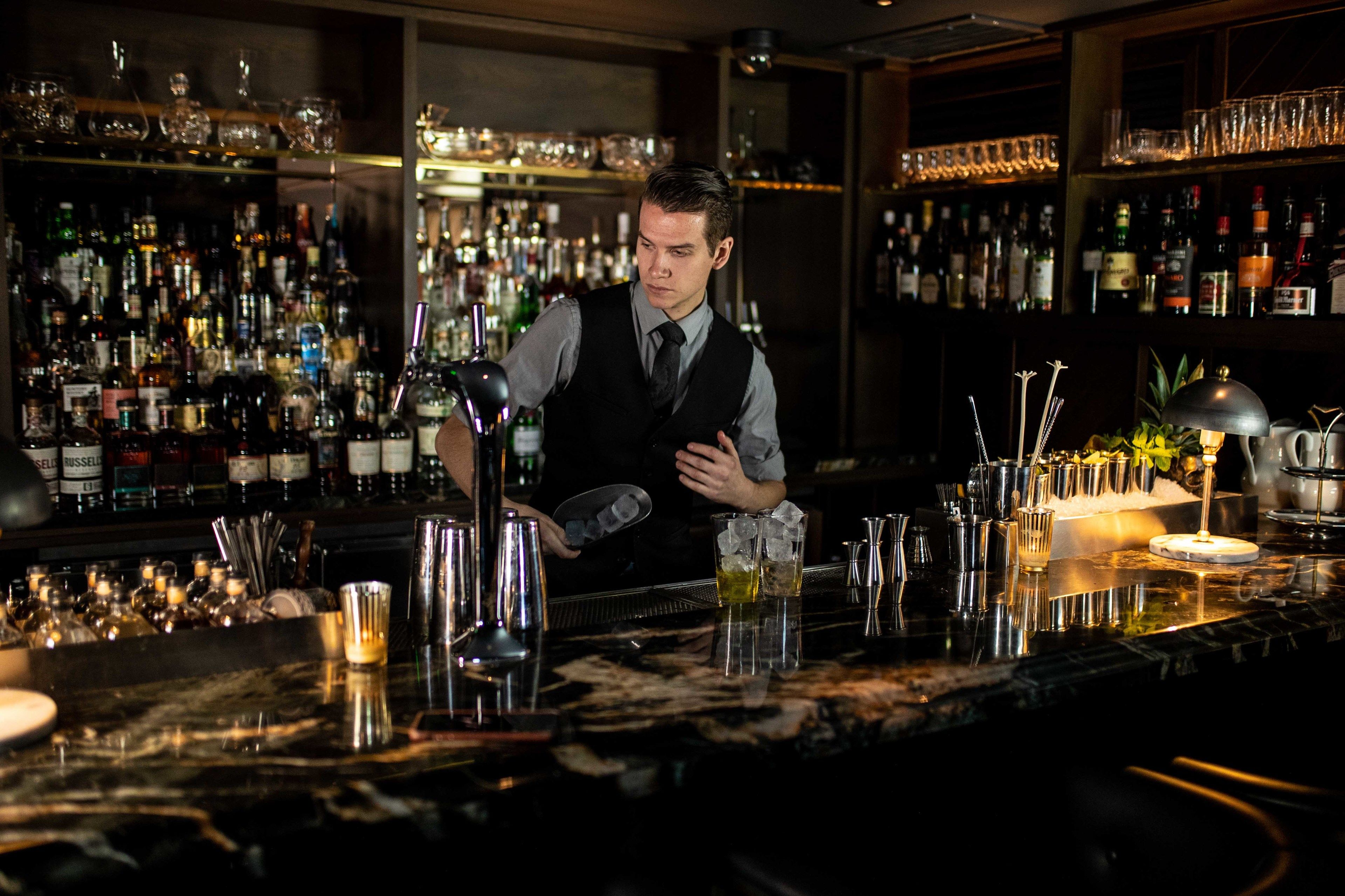 A bar with a bartender preparing drinks, shelves stocked with bottles, and a well-lit bar area.