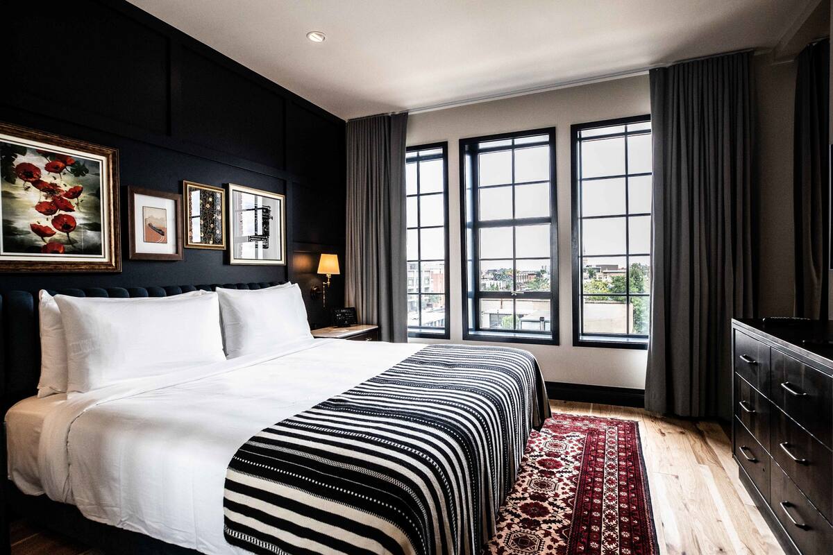 A hotel room with a large bed, a view of the city through large windows, and artwork on the wall.