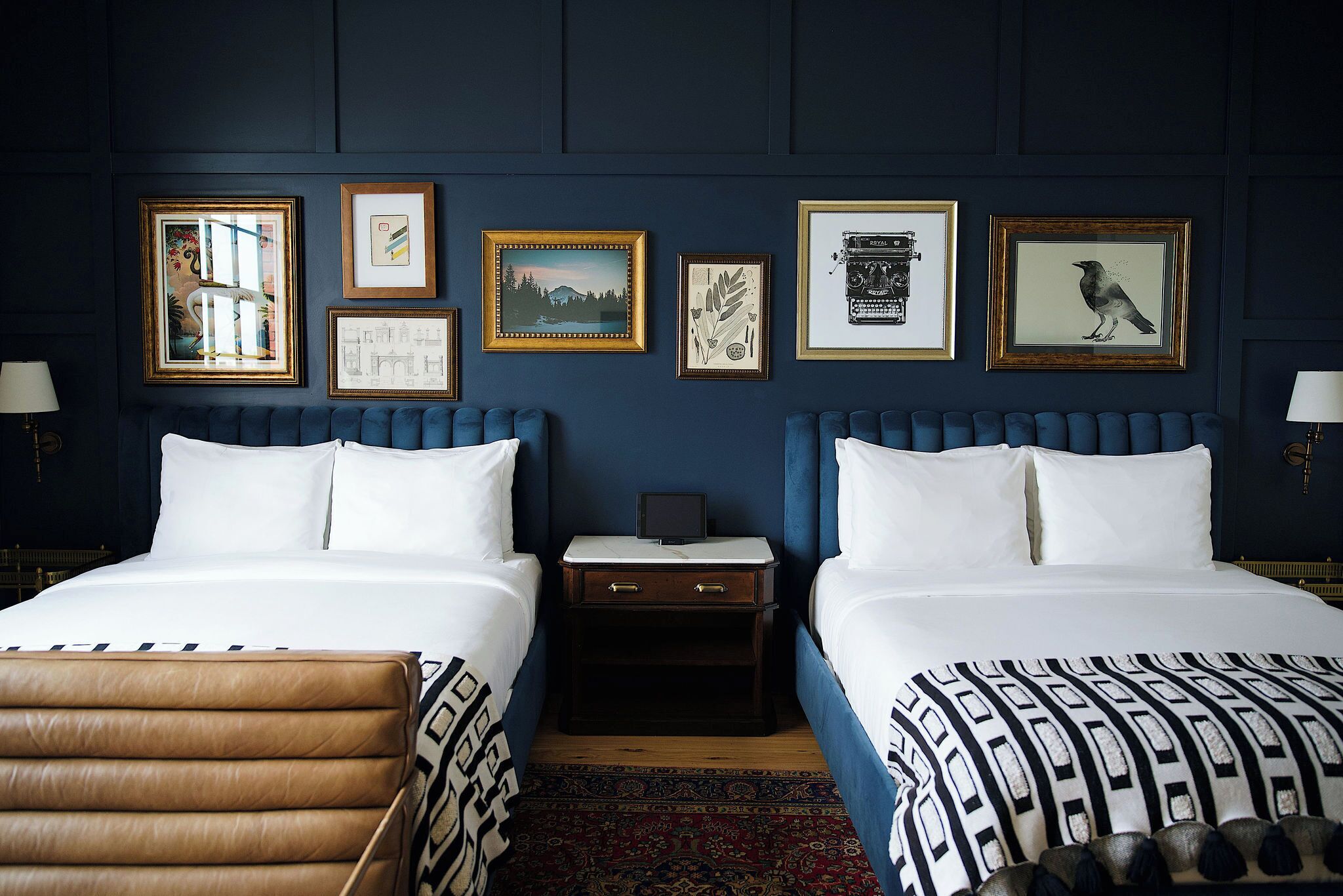A hotel room with two beds, a chest of drawers, a nightstand, and a large rug.