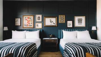 A hotel room with two beds, a dark wall with framed artwork, and a wooden nightstand.