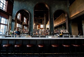 A bar with a high ceiling and arched windows, featuring a bartender and a well-stocked bar counter. - The Ramble Hotel, a Member of Design Hotels (Denver)