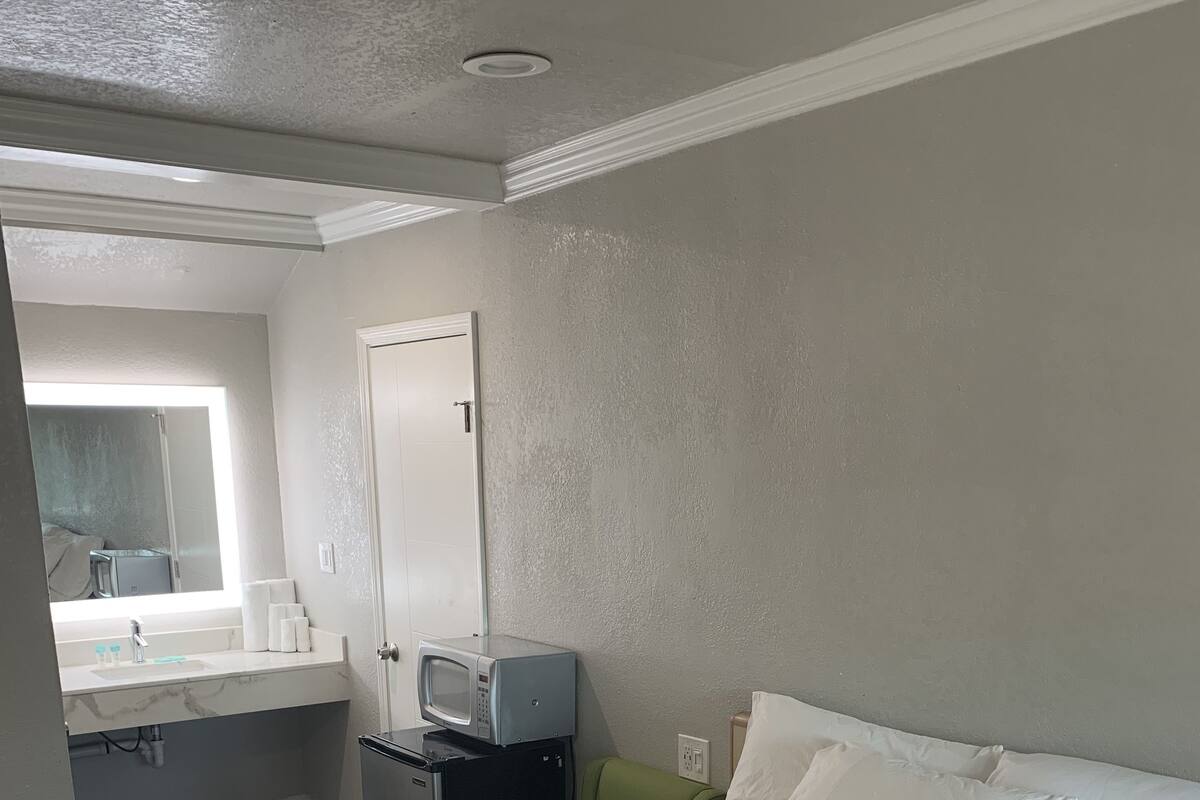 Ein Hotelzimmer mit Bett, kleinem Schreibtisch mit Mikrowelle, Badezimmer mit Waschbecken und Spiegel sowie einer Tür.