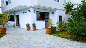 A building with a stone-paved entrance, potted plants, and outdoor seating. - Mastorakis Studios (Hersonissos)
