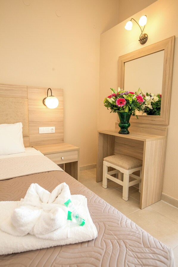 A hotel room with a bed, a nightstand, a vanity with a mirror, and a vase of flowers. - Mastorakis Studios (Hersonissos)
