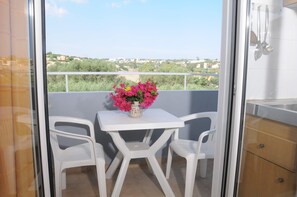 Un balcone con tavolo e due sedie, un vaso con fiori e vista sulla città.