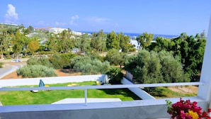 A balcony with a view of a green lawn, trees, and a distant coastline. - Mastorakis Studios (Hersonissos)