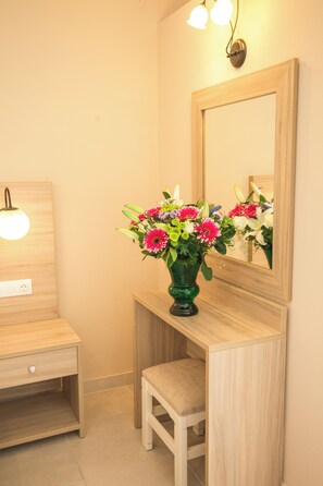 A wooden vanity with a mirror, a small stool, and a vase of flowers. - Mastorakis Studios (Hersonissos)