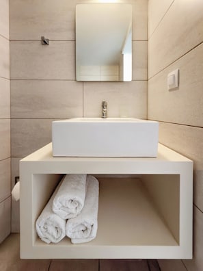 Un baño con un lavamanos blanco, un espejo y un estante para toallas.