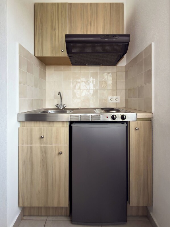 A compact kitchen with a built-in dishwasher, a stovetop with a range hood, and a sink. - Mastorakis Studios (Hersonissos)