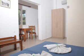 A room with a bed, a wooden chair, a wooden table, a wardrobe, and a window with a view of greenery. - Mastorakis Studios (Hersonissos)
