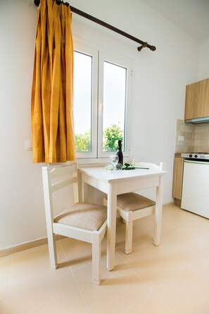 A small kitchen with a white table and chairs, a window with curtains, and a view of greenery outside. - Mastorakis Studios (Hersonissos)
