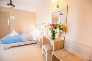 A hotel room with a bed, a bedside table with a vase of flowers, a mirror, and a wooden bench. - Mastorakis Studios (Hersonissos)