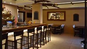 Un espace bar avec des chaises en bois, un comptoir où sont exposées des bouteilles et une horloge au mur.