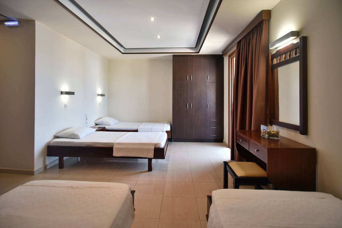 Une chambre d’hôtel avec deux lits simples, une commode en bois, un grand miroir et une armoire.