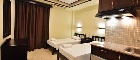 A hotel room with two beds, a small kitchenette, and a TV.