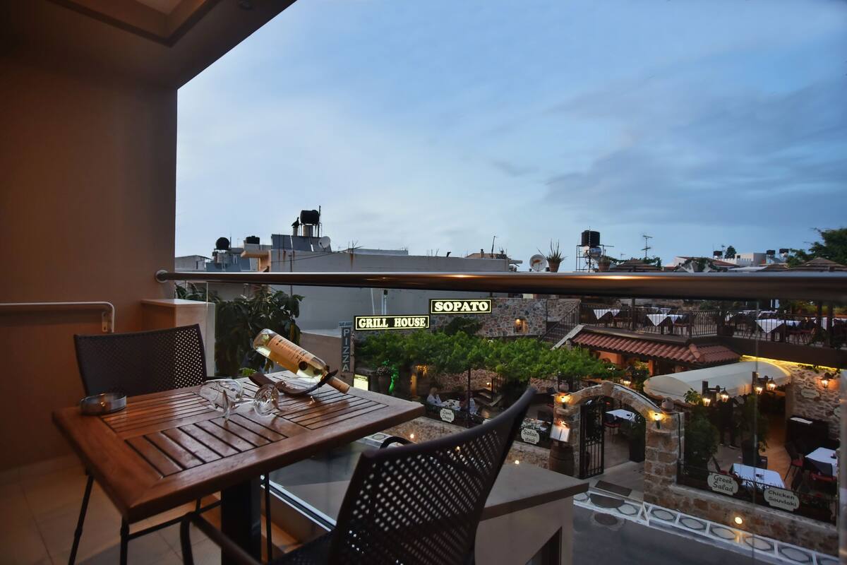 Un balcon avec une table et des chaises, donnant sur un restaurant doté d’une terrasse et offrant une vue sur le paysage urbain.