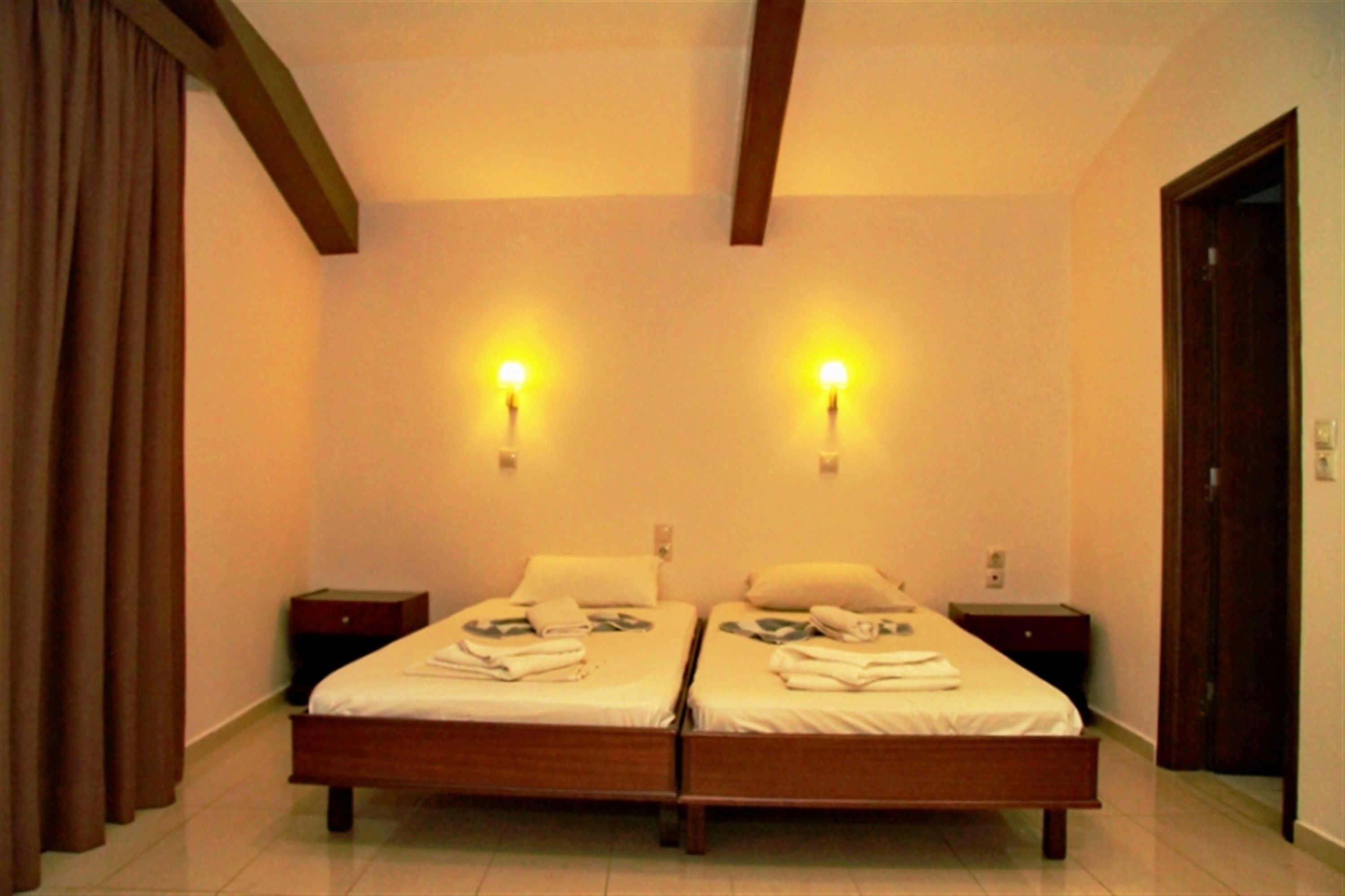 A double bed room with two bedside tables, a wooden ceiling, and a door.