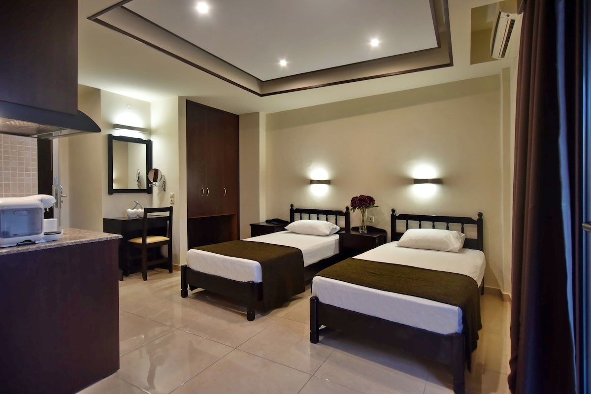 A hotel room with two single beds, a desk with a chair, a mirror, and a small table with a vase of flowers.