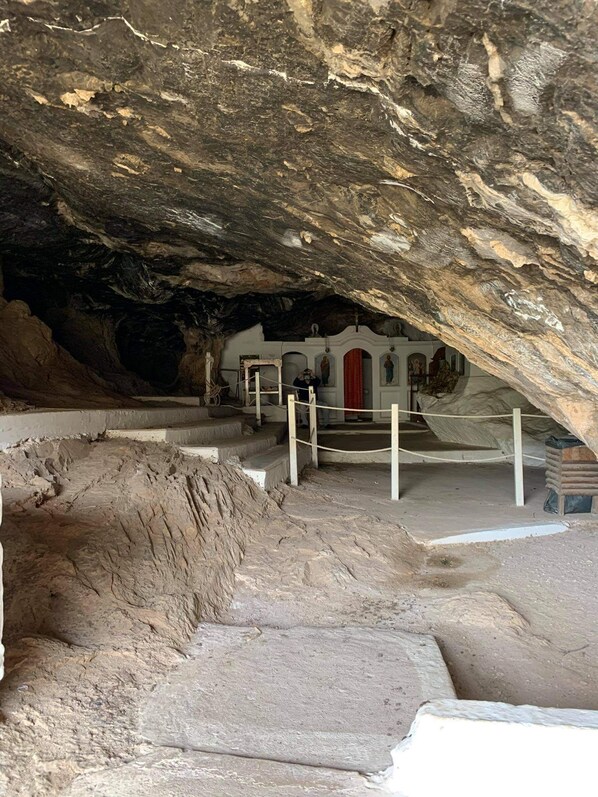 An underground church with stone walls, a red door, and a staircase leading to a small altar area. - 24 Seven Boutique Hotel (Hersonissos)