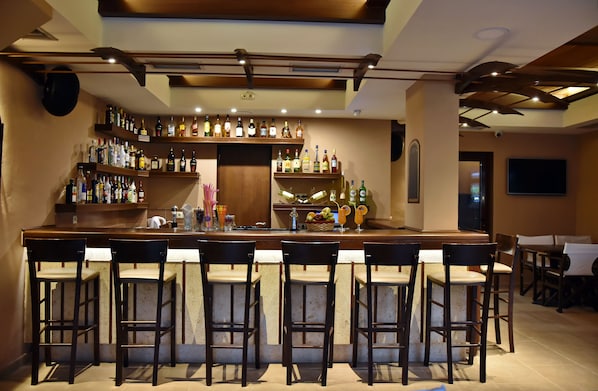 A bar area with multiple shelves of liquor bottles, a bar counter, and several bar stools. - 24 Seven Boutique Hotel (Hersonissos)