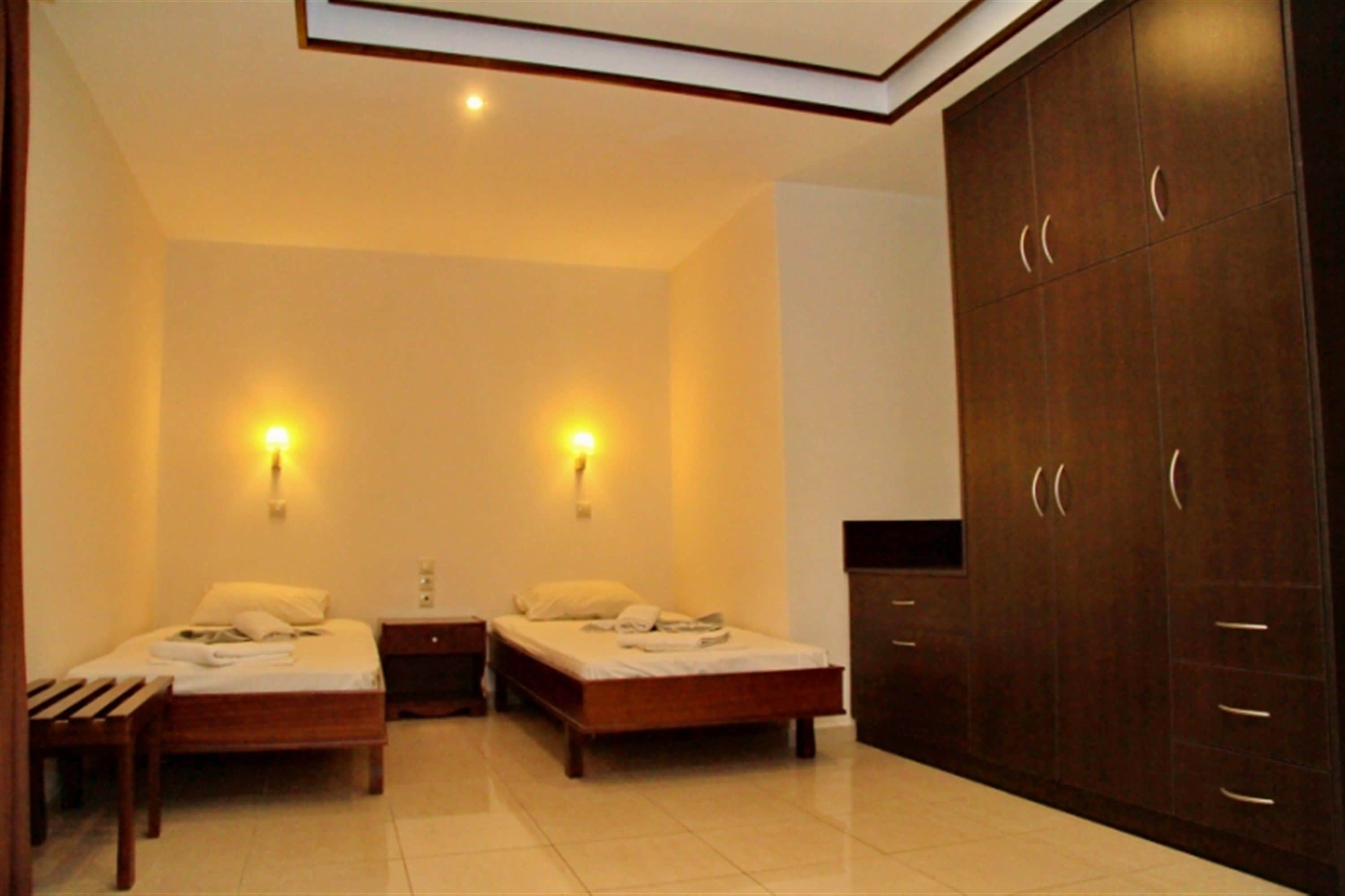 A bedroom with two beds, a wardrobe, and wall-mounted lights.