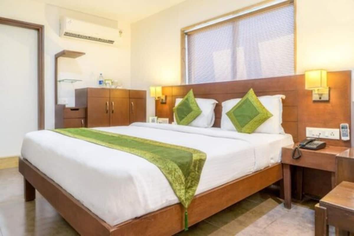 A hotel room with a wooden bed, a nightstand, a lamp, and a window with blinds.