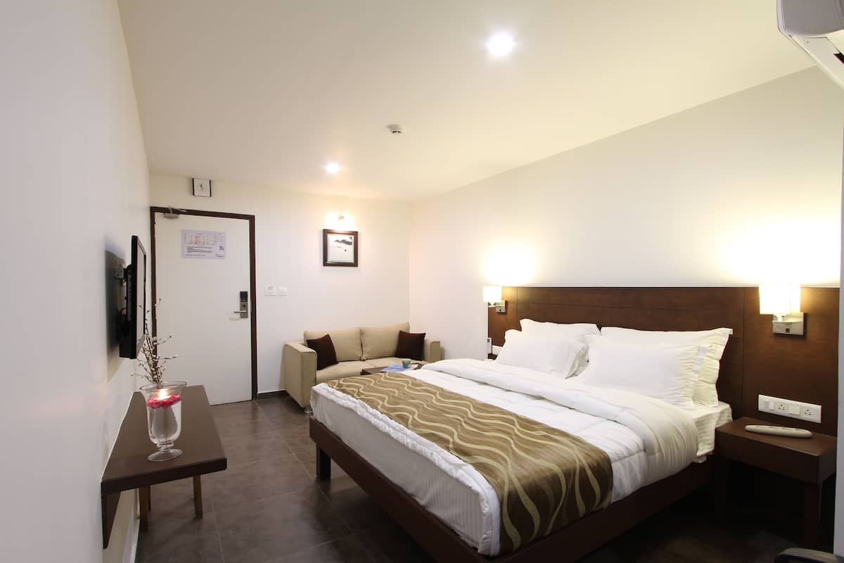 A hotel room with a bed, bedside table, nightstand, and a small table with a vase.