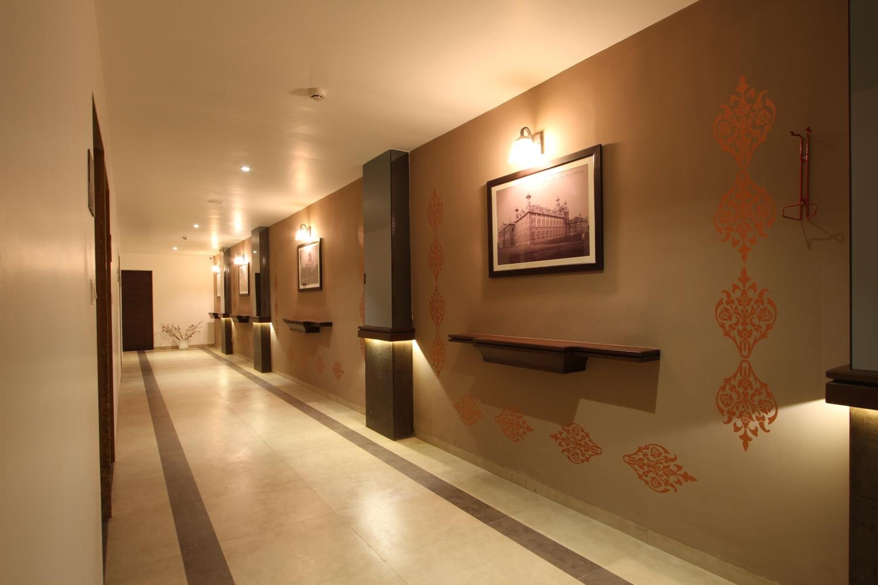 A hallway with a long, narrow layout, featuring wall-mounted light fixtures and framed pictures.
