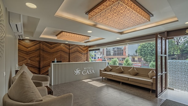 A hotel reception area with a modern design, featuring a reception desk, seating area, and large windows offering a view of the cityscape. - Hotel Casa (Vadodara)