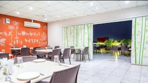 A restaurant with indoor and outdoor seating, a tiled floor, and a wall with a bamboo design. - Hotel Casa (Vadodara)