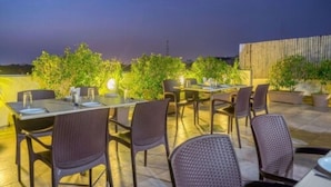 An outdoor dining area with tables and chairs, surrounded by greenery and a wooden fence. - Hotel Casa (Vadodara)