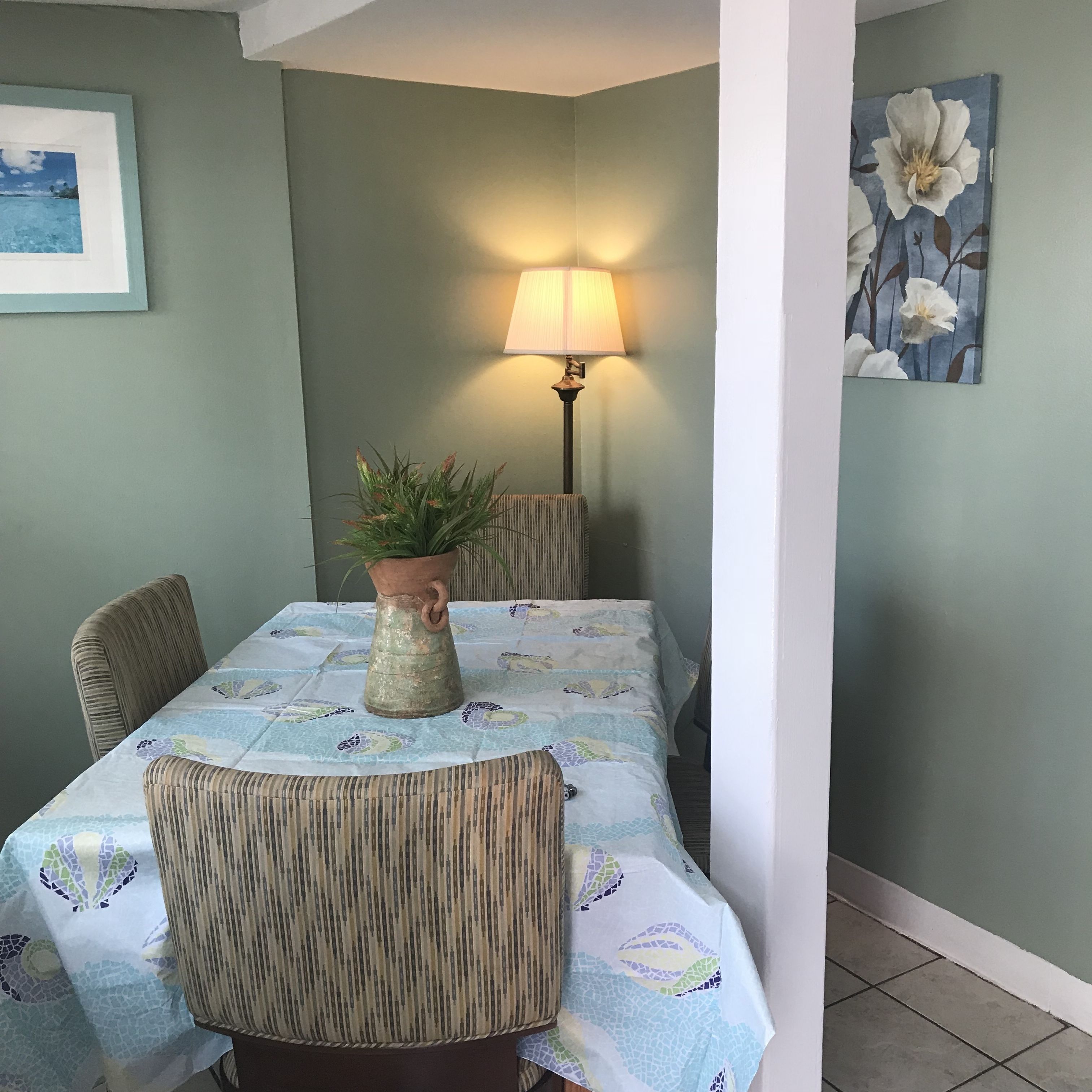 A dining area with a table covered by a patterned tablecloth, a potted plant, and a lamp.