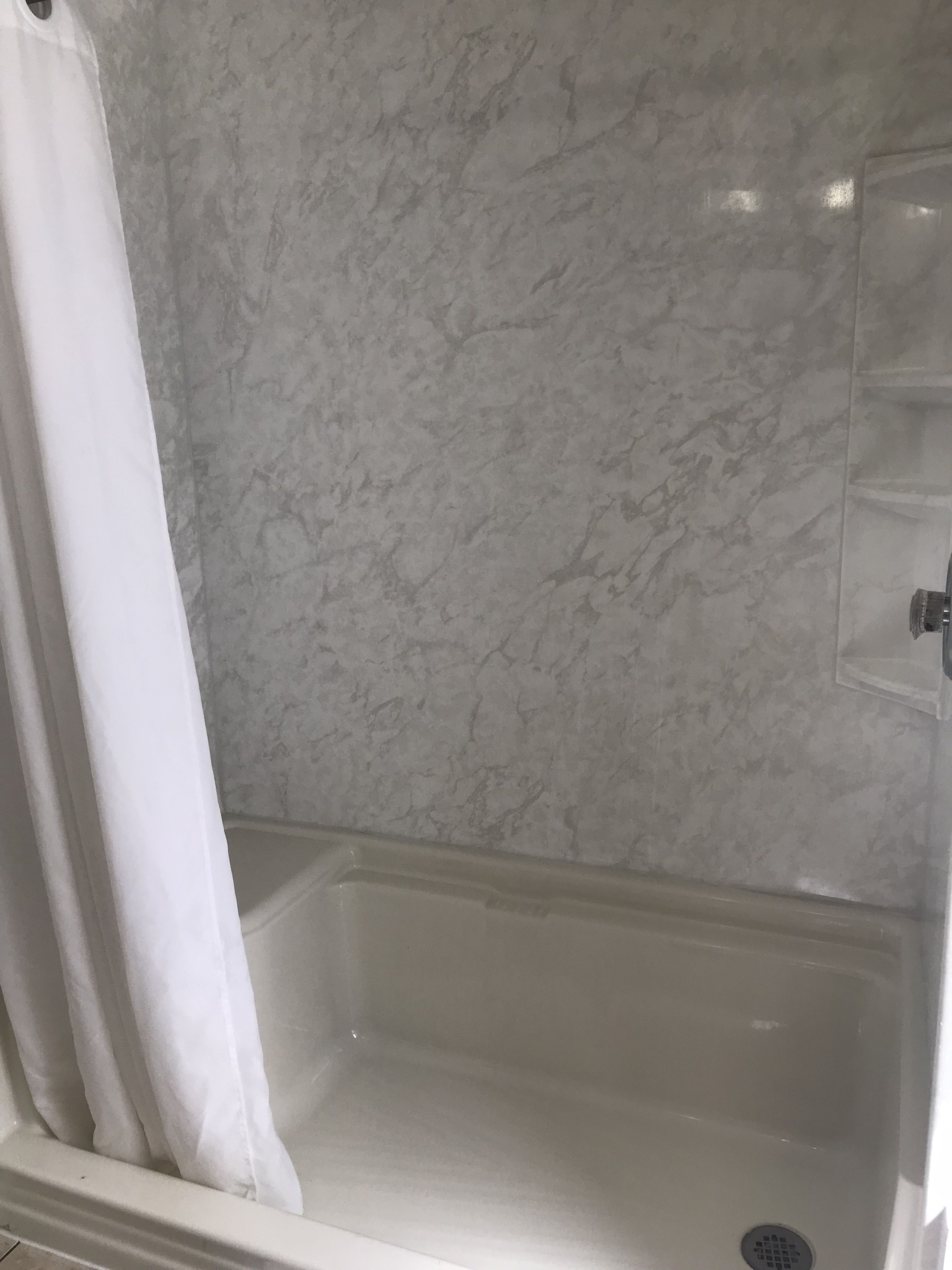 A bathroom with a white shower curtain, a marble wall, and a white bathtub.