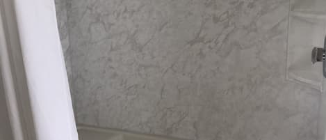 Ein Badezimmer mit weißer Duschvorhang, Marmorwand und Badewanne in Weiß.