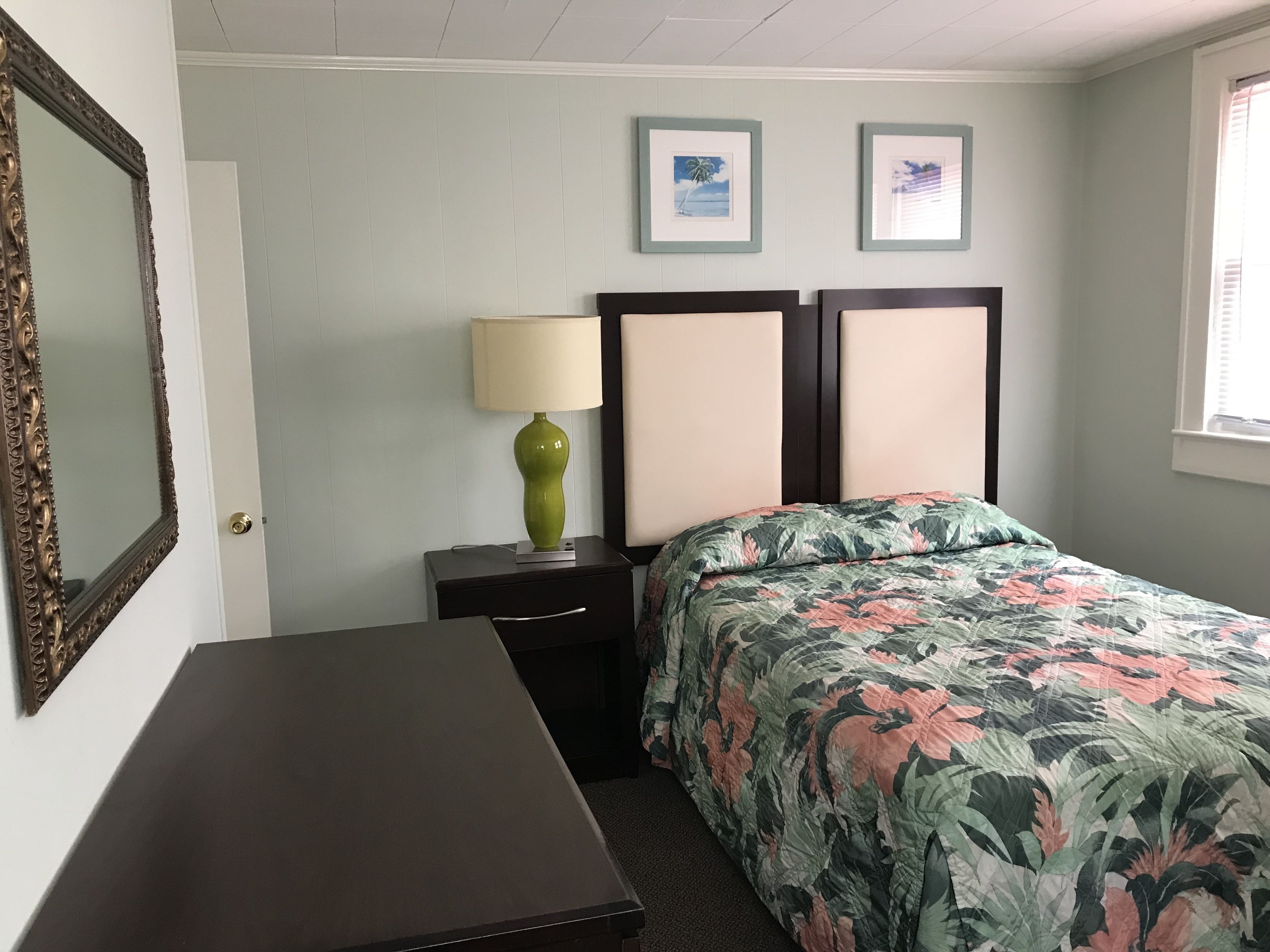 Een hotelkamer met een bed, nachtkastje met lamp, een dressoir en twee ingelijste foto's aan de muur.