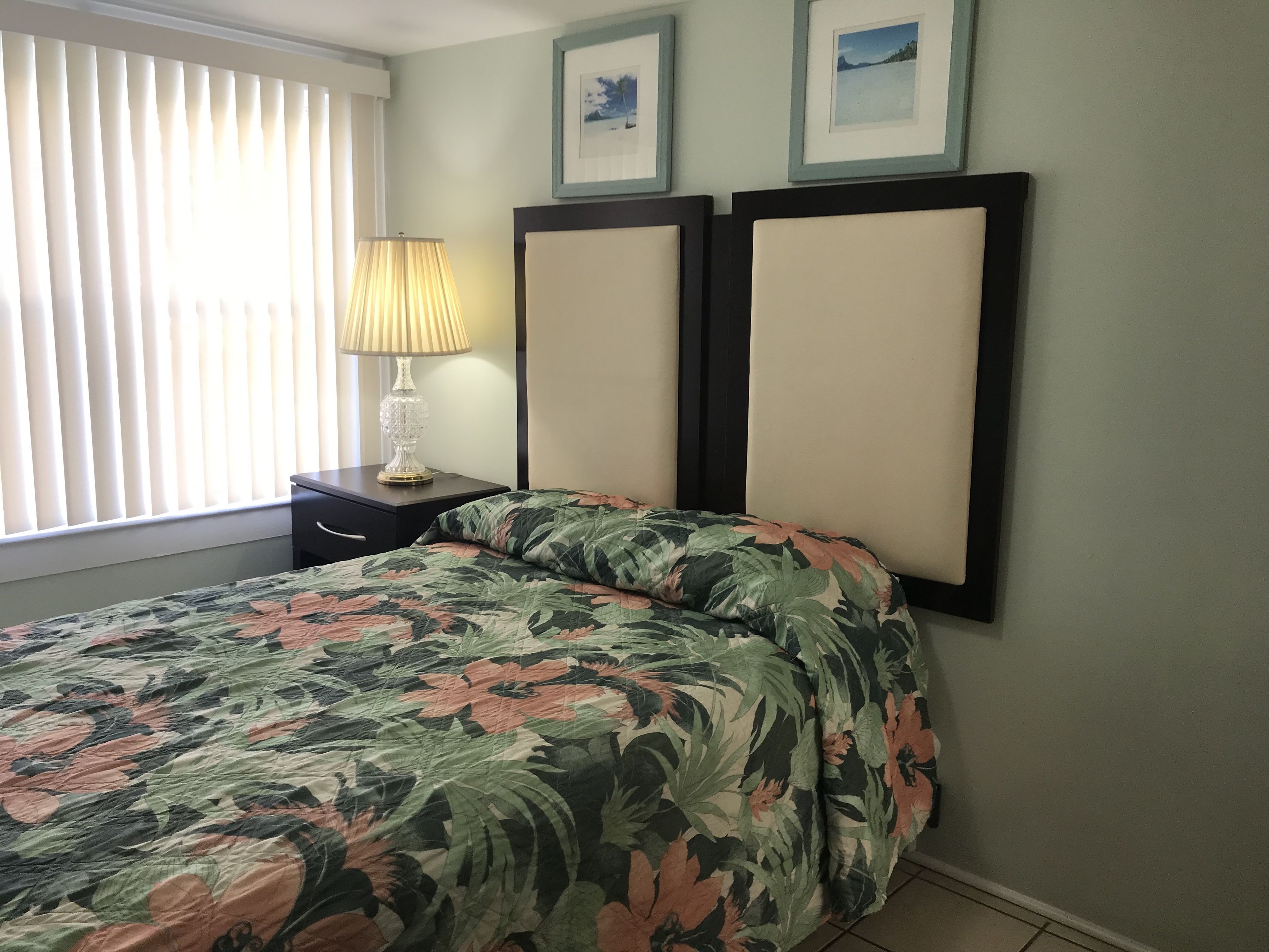 A bedroom with a bed, a nightstand, a lamp, and two framed pictures on the wall.
