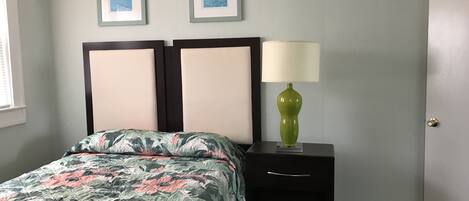 A bedroom with a floral bedspread, a nightstand with a green lamp, and two framed pictures on the wall.