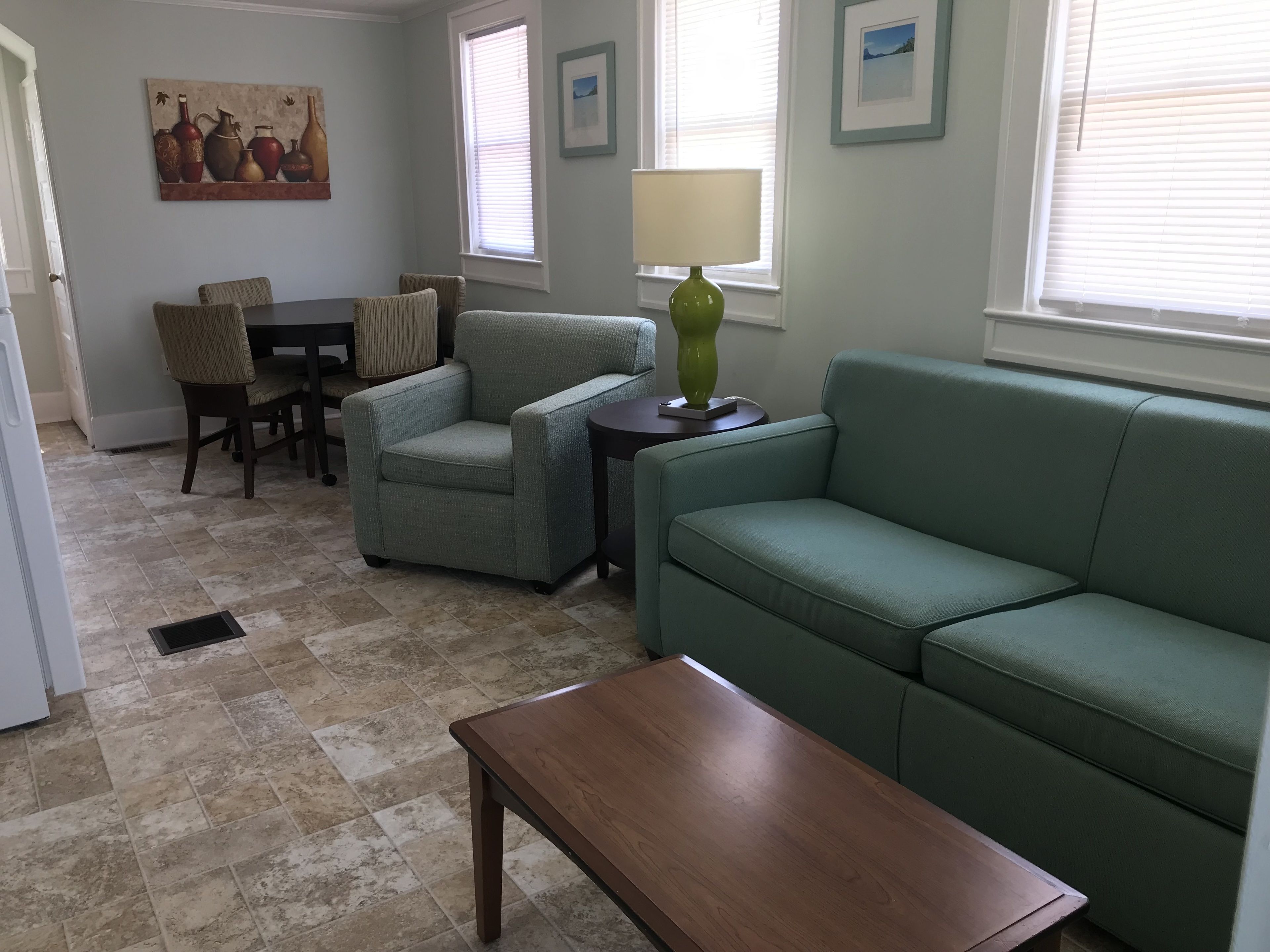 A living room with a green sofa, a wooden coffee table, and a dining area with chairs and a table.