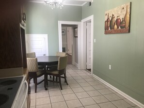 Un comedor con una mesa redonda y cuatro sillas, una araña y un cuadro en la pared.