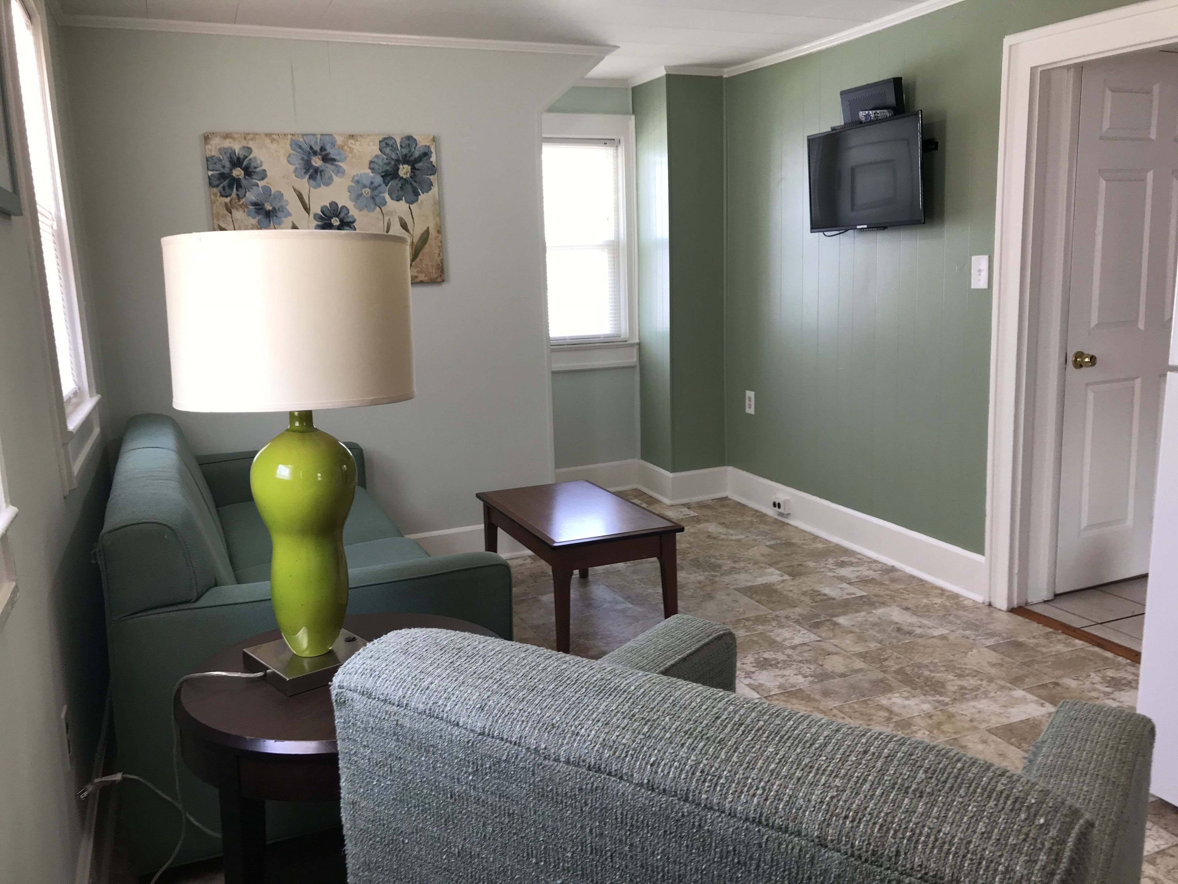 A living room with a green sofa, a green armchair, a small wooden table, and a floor lamp.