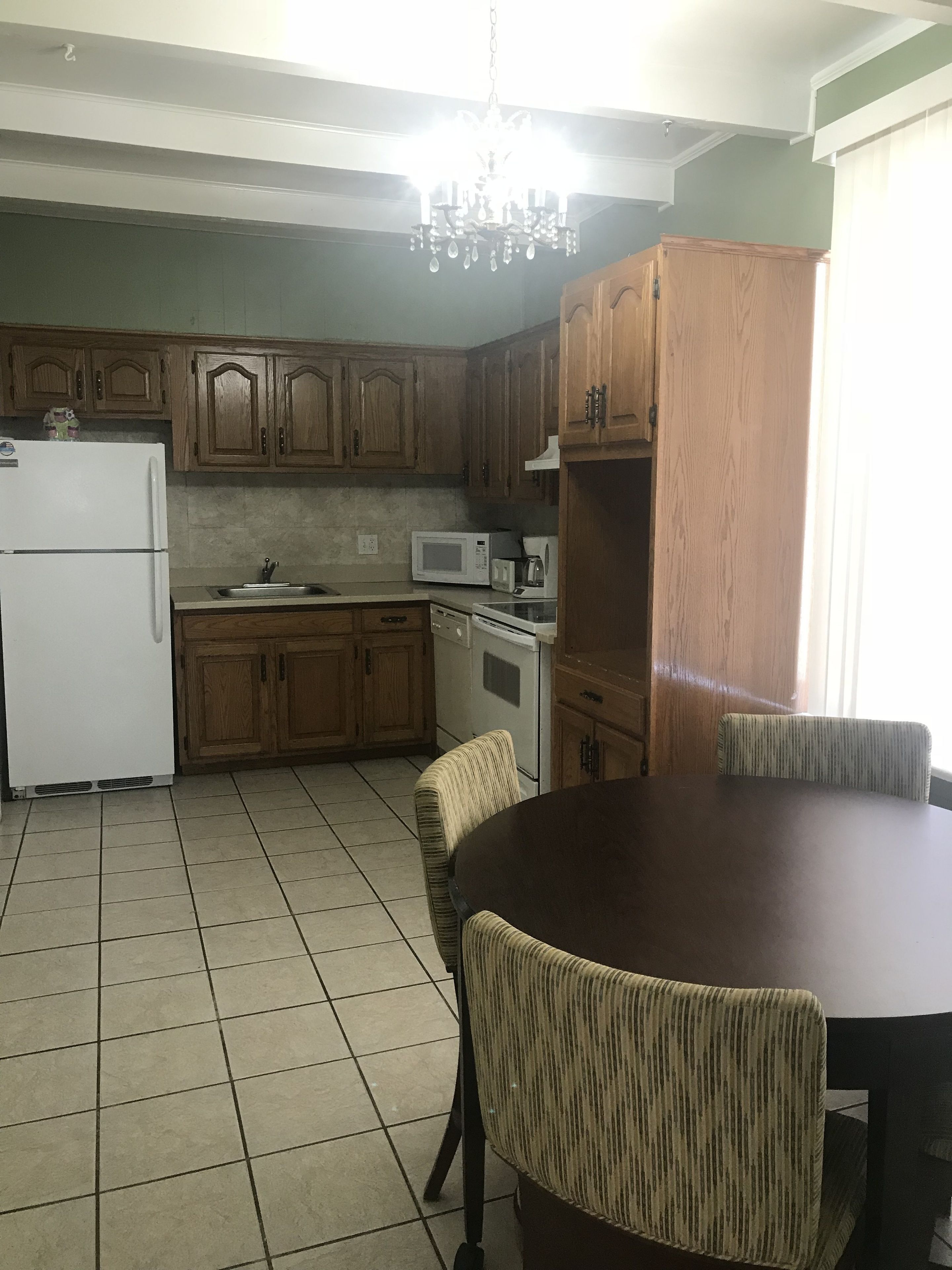 A kitchen with wooden cabinets, a white refrigerator, a microwave, and a dining table with chairs.
